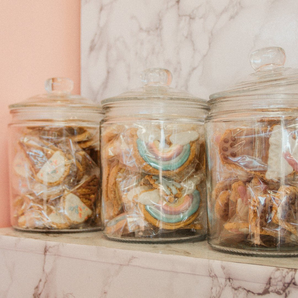 Brightly coloured dog cookie treats in glass jars on a marble shelf at Little Ellie Boutique an Australian dog brand