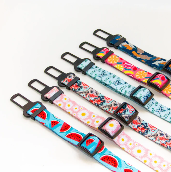 Adjustable dog car restraints in bright and colourful prints are lined up diagonally across the screen from Little Ellie, an Australian dog brand