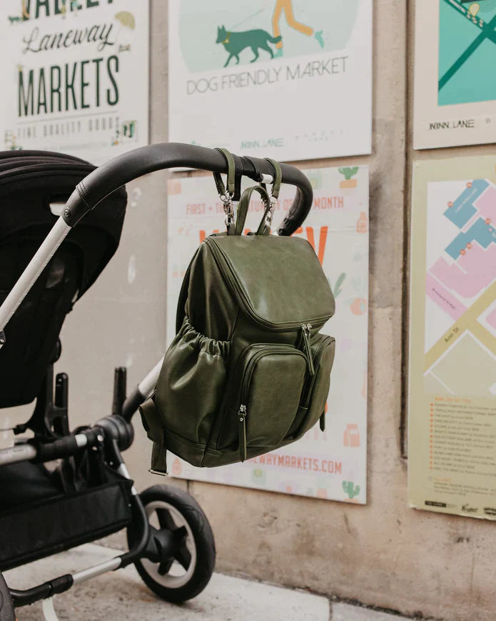 Olive green OiOi Baby Nappy Backpack hanging from a black stroller handle. 